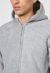 Grijze fleece hoodie met een voorrits, gevoerd met een zachte binnenstof, voorzien van een geribde kraag en capuchon met een contrasterende textuur.