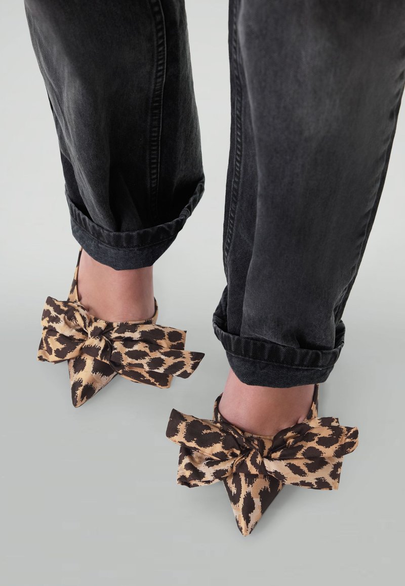 Des mules en tissu imprimé léopard avec un grand nœud présentent un bout pointu et sont portées avec un jean noir retroussé.