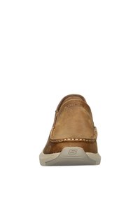 Chaussure en cuir marron à enfiler avec une finition lisse, semelle en caoutchouc beige, couture décorative le long du bord et un logo à l'arrière.