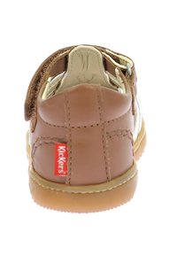 Zapato infantil de cuero marrón con una correa de Velcro, acentos en crema y suela de goma. Etiqueta de logo roja en el talón.