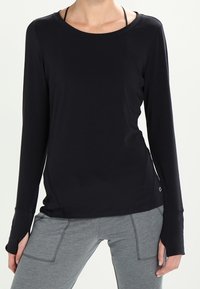 Svart långärmad topp med rund halsringning, mjuk textur och tumhål i ärmarna, kombinerad med grå tajta byxor.