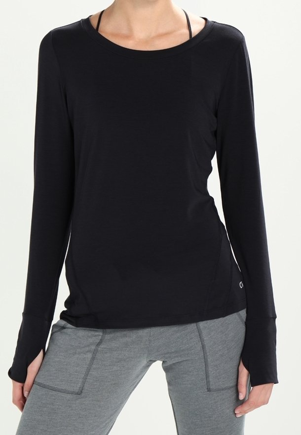 Svart långärmad topp med rund halsringning, mjuk textur och tumhål i ärmarna, kombinerad med grå tajta byxor.