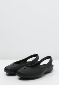 Chaussures noires à enfiler avec un bout arrondi, fabriquées en matériau flexible, dotées d'un design à talon ouvert et d'accents minimalistes. Texture lisse.