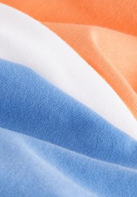 Bavlněná látka v pruhovaném vzoru oranžové, bílé a modré barvy, která se vyznačuje jemnou texturou a hladkým povrchem, vrstvená s mírnými sklady pro hloubku.