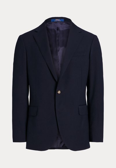 Μπλε σκούρο σακάκι με ένα χρυσό κουμπί, γιακά με σχισμή και δύο μπροστινές τσέπες. Λεία εσωτερική φόδρα, εφαρμοστή γραμμή, κλασικός σχεδιασμός.