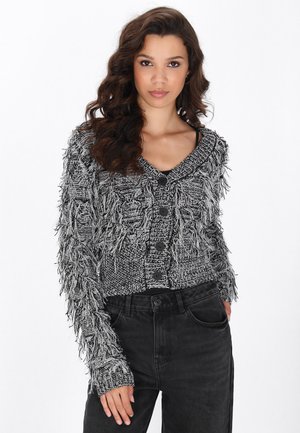Cardigan a frange in bianco e nero con un design a maglia testurizzata, dotato di scollatura a V e cinque bottoni neri sul davanti.