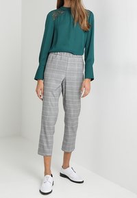 Tealfärgad blus med spetsdetaljer vid axlarna, kombinerad med grå rutiga capribyxor och vita brogueskor.