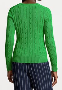 Suéter verde de punto trenzado con patrón texturizado, dobladillo y puños acanalados, diseño ajustado, combinado con pantalones a rayas azul marino.