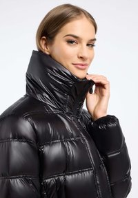 Zwarte pufferjack met een hoge kraag en glanzende afwerking. Voorzien van een ritssluiting, geruit quilting en ribboorden voor extra warmte.