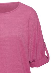 Locker sitzendes pinkes Oberteil mit Rundhalsausschnitt und kurzen, gerollten Ärmeln. Der Stoff hat eine strukturierte Optik, die visuelles Interesse schafft.
