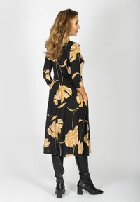 Czarna sukienka w kwiaty z dużymi beżowymi kwiatami, z długimi rękawami i zwiewnym fasonem, połączona z czarnymi kozakiem na wysokim obcasie do kolan.