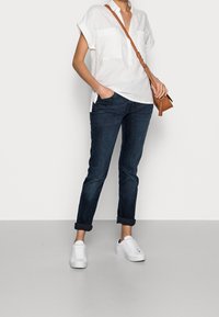 Biała, krótko rękawowa koszula lniana z dwiema przednimi kieszeniami, w połączeniu z ciemnoniebieskimi, podwiniętymi dżinsami oraz białymi trampkami. Brązowa torba na ramię.