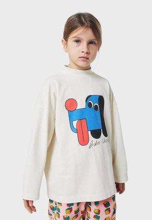 T-shirt a maniche lunghe di colore crema realizzato in cotone, con una grafica colorata di un cane in blu, rosso e nero. Tessuto morbido con una vestibilità comoda.