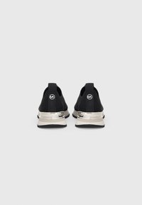 Sneaker neri con tomaia testurizzata, dettagli metallici sul tallone e linguette per il pull. Presentano suola beige a contrasto e un logo rotondo sulla parte posteriore.