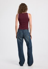 Maroon sleeveless top with pink straps, paired with loose-fitting blue denim jeans featuring two back pockets and a faded finish.