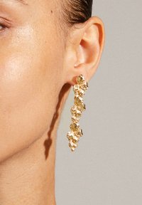 Goldfarbene Tropfenohrringe mit einer Kette aus strukturierten, blütenförmigen Gliedern, die mit einem polierten Finish und komplizierten Details glänzen.