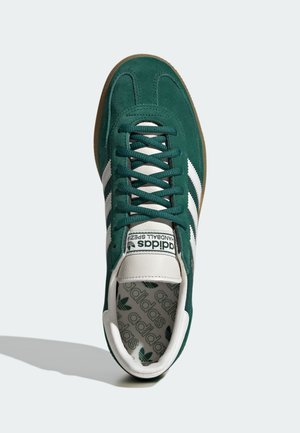 Baskets Adidas en daim vert avec des bandes blanches, une étiquette blanche sur la languette et une semelle intérieure de marque, vues de dessus sur un fond clair.