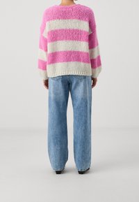 Pull tricoté rayé rose et blanc, avec un corps large et des manches longues. Associé à un jean bleu clair à coupe ample.