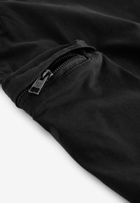 Joggers de tela negra con un bolsillo con cremallera, diseño estilizado, textura suave y detalles de costura a lo largo de los bordes.