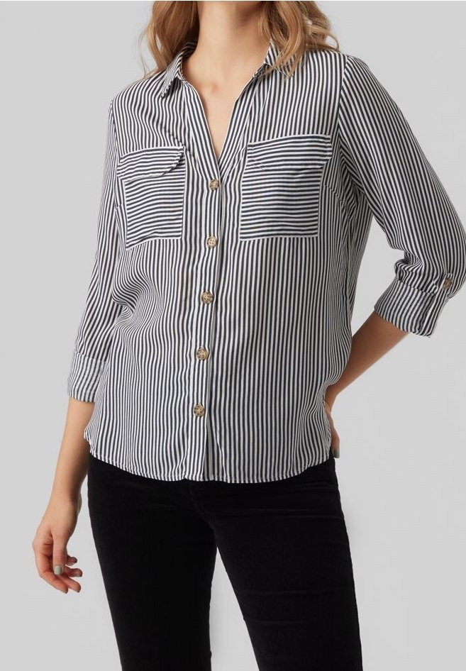 Femme portant une chemise boutonnée à rayures verticales noires et blanches avec deux poches poitrine à rayures horizontales et manches retroussées.