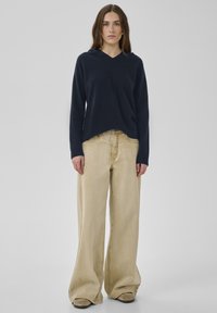 Marineblaue Strickpullover mit V-Ausschnitt, kombiniert mit lockeren, hellbeigen Jeans mit weitem Bein. Das Outfit besticht durch weiche Texturen und ein lässiges Design.