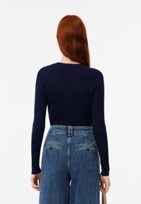 Top a maniche lunghe a costine color navy abbinato a jeans in denim blu a vita alta con tasche posteriori, un dettaglio logo e una vestibilità comoda.