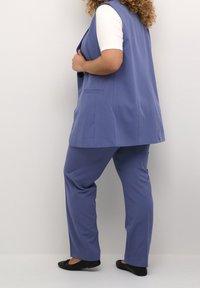 Niebieska kamizelka z kołnierzykiem, zestawiona z dopasowanymi spodniami. Miękka tkanina, dopasowany krój i boczne kieszenie. Noszona z czarnymi balerinami.