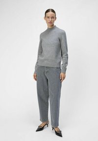 Suéter gris de punto con patrón texturizado, cuello redondo, puños acanalados, combinado con jeans gris de corte holgado y tacones negros de puntera afilada.