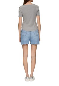 Grijze korte mouwen top gecombineerd met lichtblauwe denim shorts met een rafelige zoom en twee achterzakken, gedragen met witte schoenen.