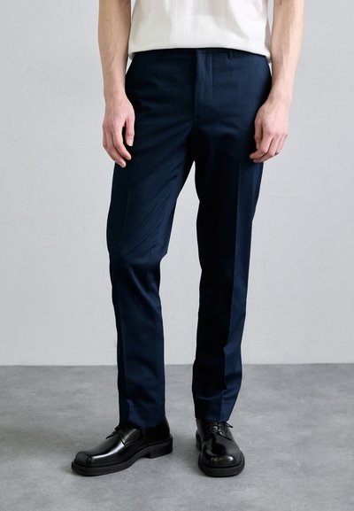 Pantalones de corte navy hechos de tejido suave, con un corte recto y pliegues frontales, combinados con zapatos de cuero negros.