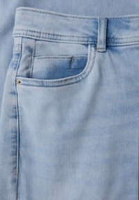 Tissu en denim bleu clair avec une poche visible, des coutures cousues et une légère texture de décoloration près de la poche. Doté d'une taille standard.