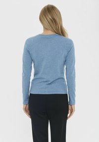 Mėlynas medvilnės marškinis ilgomis rankovėmis su apvaliu iškirpimu, prigludusi siluetas ir be siūlių pečiai; derinamas su tamsiomis kelnėmis.