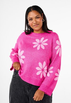 Różowy sweter dzianinowy z długimi rękawami, ozdobiony dużymi białymi wzorami kwiatowymi oraz prążkowanym dekoltem i mankietami. Casualowy, luźny krój.