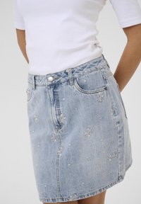 Jupe en denim bleu clair, ornée de détails brodés floraux, avec cinq poches, passants de ceinture, fermeture à bouton et un ourlet légèrement évasé.