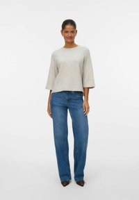Helehall kootud sviiter, laiad varrukad, koos siniste sirgete säärtega denim-pükstega ja terava nina pruunide kingadega. Minimalistlik disain, ilma mustriteta.