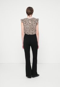 Bluza s leopard uzorkom i volanima, crne zakovane hlače i crna obuća. Pogled straga na jednostavnoj bijeloj pozadini.