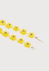 Perles en forme de fleur jaune avec des centres bleus et de petites perles blanches, enfilées ensemble et terminées par des fermoirs en argent sur un fond blanc.