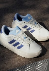 Bijele tenisice s plavim detaljima i tri bočne pruge, s glatkim kožnim gornjim dijelom i teksturiranom gumenom potplatom.