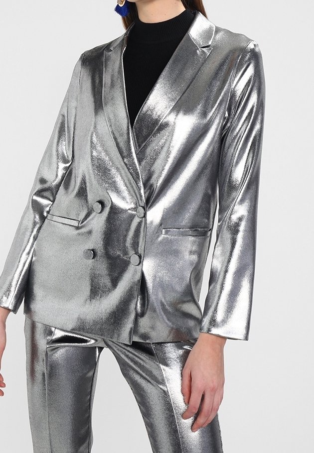 Stříbrný metalický blazer se dvěma knoflíky, klopovými límci a dvěma předními kapsami. Spárovaný s odpovídajícími metalickými kalhotami, které mají lesklý povrch.