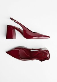 Glänzende dunkelrote Slingback-Absätze mit spitzer Zehe und Blockabsatz, aus seitlicher und oberer Perspektive vor einem weißen Hintergrund gezeigt.