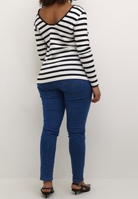 Haut à manches longues à rayures noires et blanches avec un décolleté profond dans le dos, associé à un jean skinny bleu et des sandales plates noires.