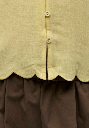 Tissu jaune texturé avec bord festonné et deux petits boutons sur tissu marron foncé plissé.