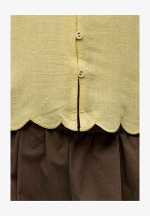 Gul teksturert stoff med bølget kant og to små knapper over mørkebrunt rynket stoff.