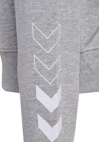 Szary materiał bluzy z białym wzorem chevron na lewym rękawie. Materiał wydaje się miękki i teksturowany, z klasycznym dekoltem okrągłym.