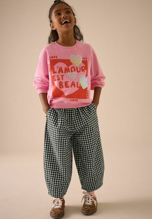 Sweat-shirt rose avec le design "L'amour est beau" ; pantalon large à carreaux vichy vert et noir ; chaussures marron à pois ; style décontracté.