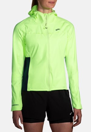 Giacca da corsa gialla neon con cappuccio, zip frontale e pannelli laterali scuri. Presenta maniche lunghe e il logo "Brooks" sulla manica inferiore.