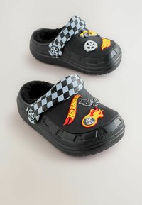 Black rubber clogs with a soft fur lining, adorned with colorful "Hot Wheels" graphics, a checked strap, and flame motifs.