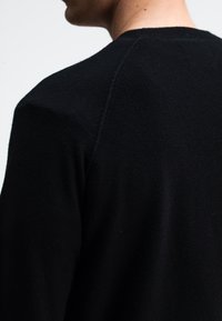 Schwarzer Strickpullover mit rundem Ausschnitt und Raglanärmeln, der in einer Nahaufnahme eine weiche Textur und ein nahtloses Design zeigt.