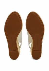Sandalias de cuña abiertas con parte superior de lienzo blanco, tacón tejido natural y suela de goma marrón con agarre texturizado. Logo de la marca en la suela.