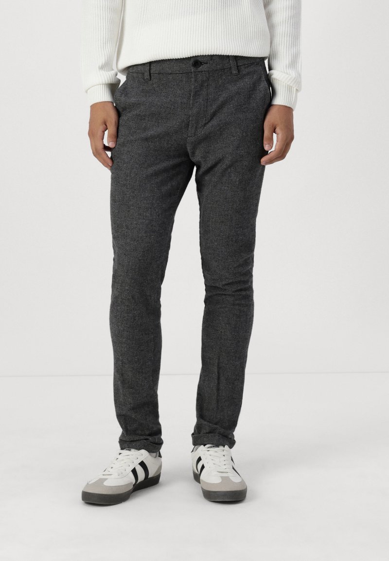 Pantalones grises texturizados con un ajuste slim, con cierre de botón y bolsillos, combinados con zapatillas deportivas blancas y grises.